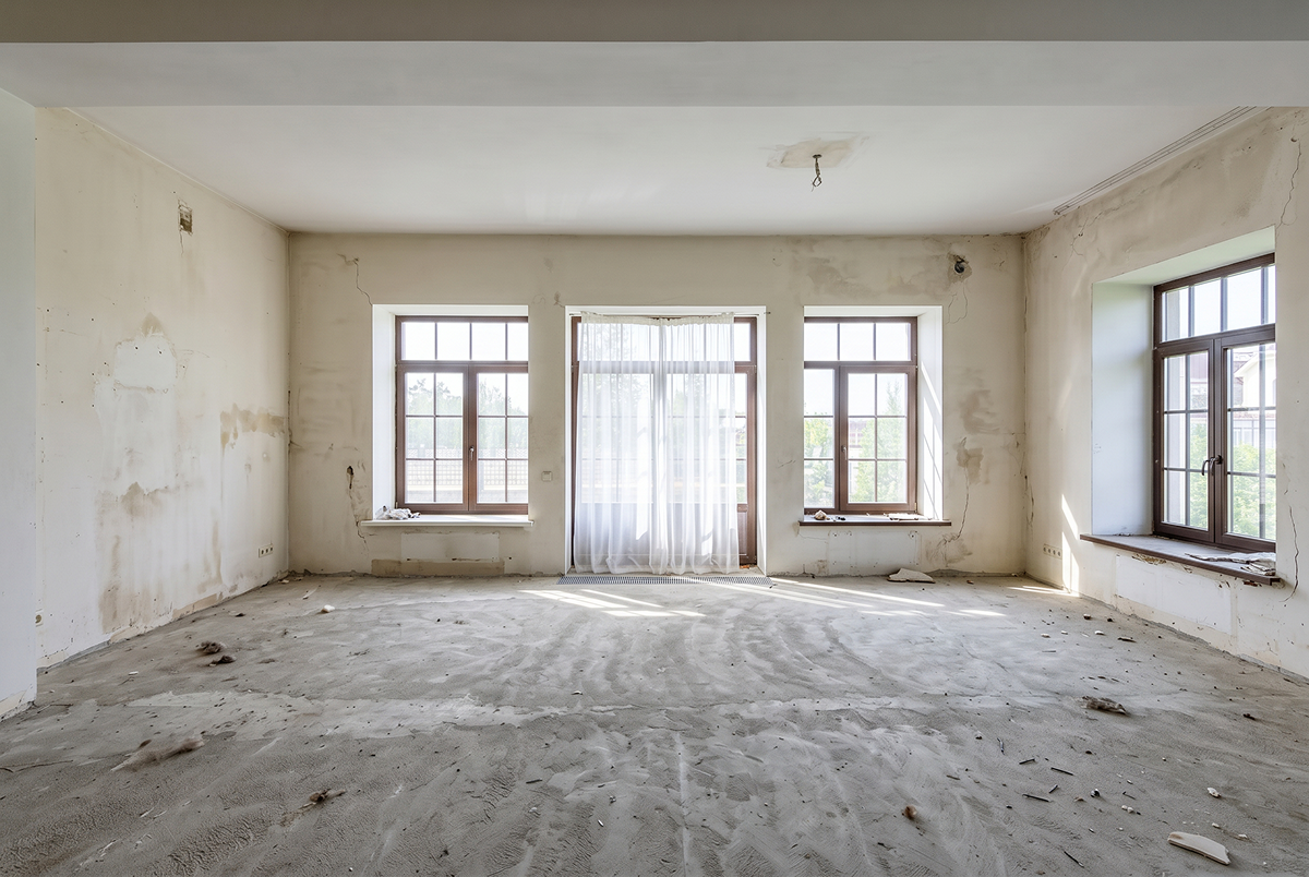 Empty living room mid-renovation, bare concrete subfloor and unfinished walls